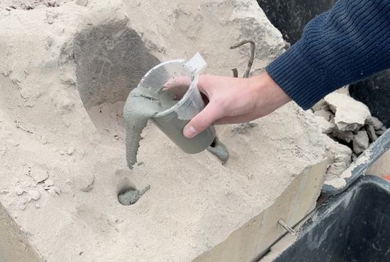 Ein Arbeiter füllt angerührten Betonamit in zuvor gebohrte Löcher eines Betonschornsteins ein.