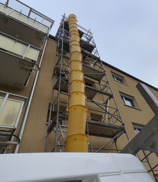 Schuttrutsche an einem eingerüsteten Mehrfamilienhaus zur sicheren Entsorgung von Schornstein-Schutt.